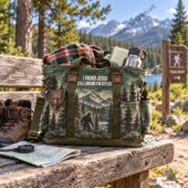 Green canvas tote bag with a Bigfoot and mountain print on a wooden trail bench.