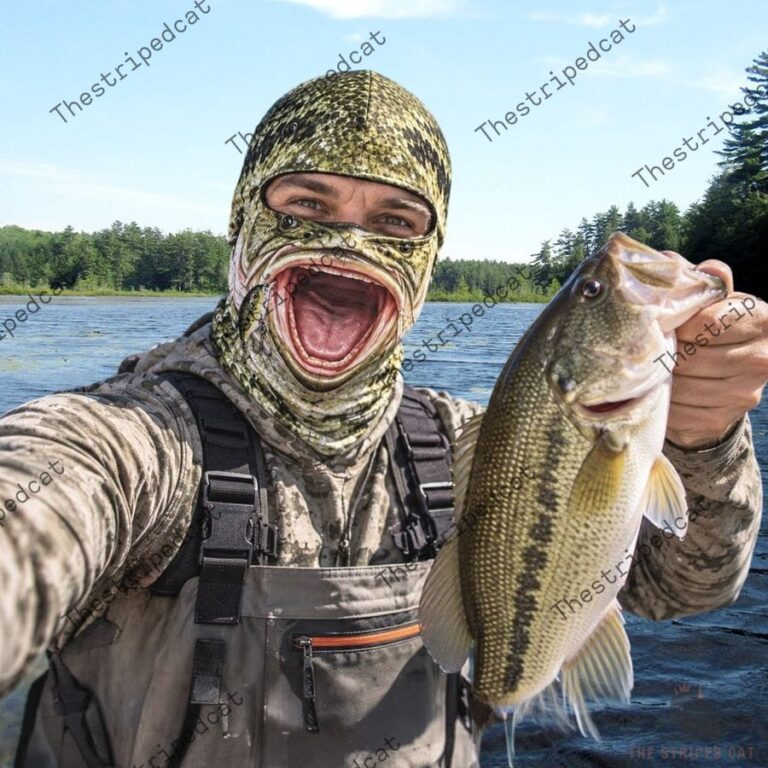 Angler wearing a bass fish mouth face mask holding a freshly caught largemouth bass by the lake.